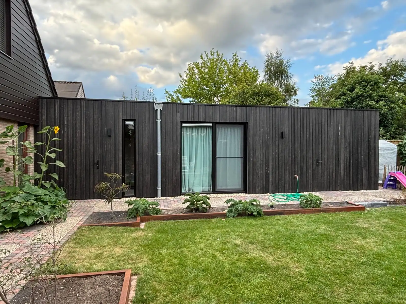 Aanbouw met een zwart houten gevel aan de tuinzijde, met gazon ervoor